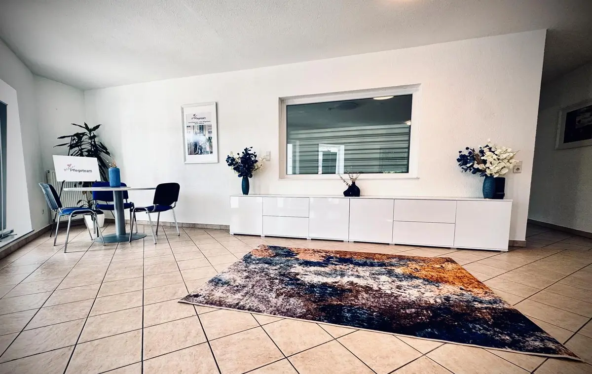 Beratungsbereich mit rundem Tisch, blauen Stühlen, Logo-Schild und Blumendekoration