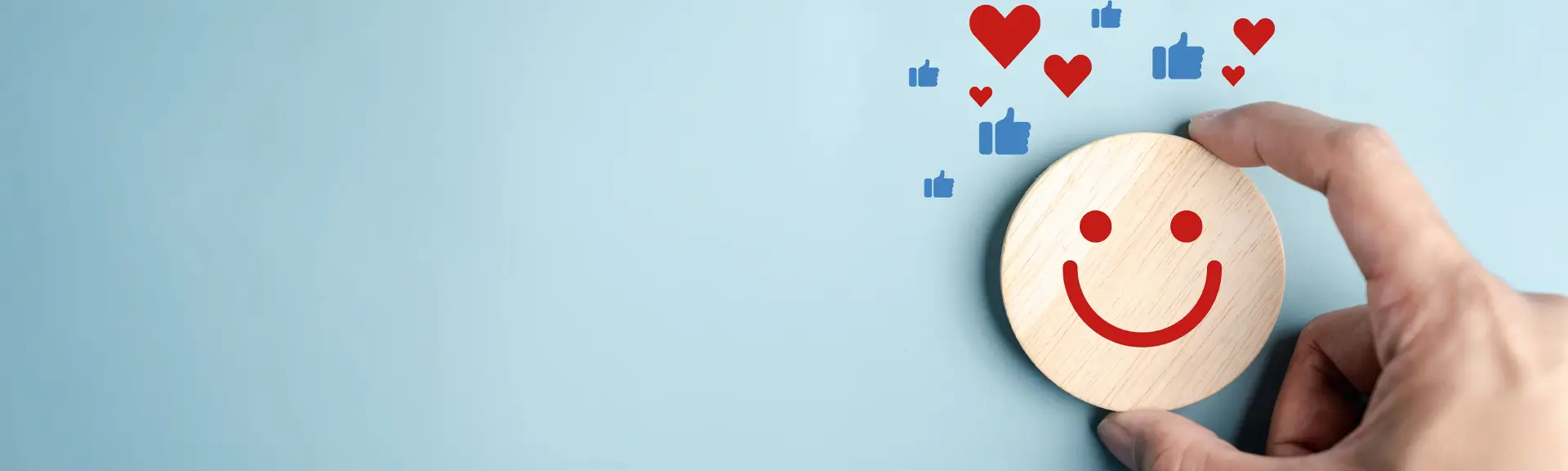 Hand hält rundes Holzstück mit lachendem Gesicht und darüber schwebende rote Herzen und blaue Like-Symbole
