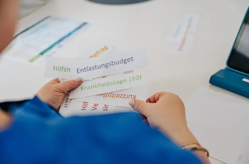 Hände halten beschriftete Karten zu Pflegeleistungen über einem Tisch