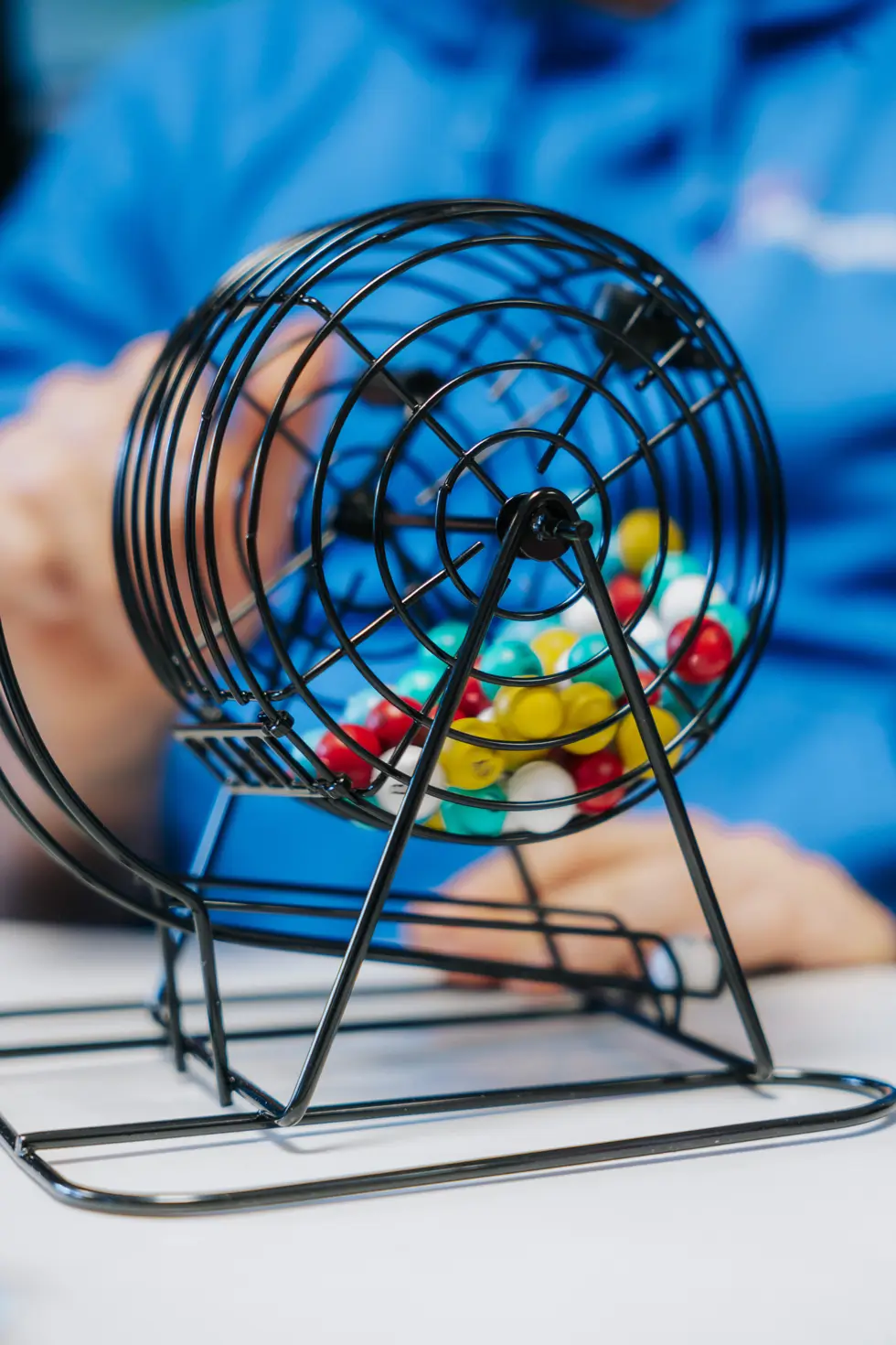 Drehbarer Metallkorb mit bunten Bingo-Kugeln vor verschwommenem Hintergrund