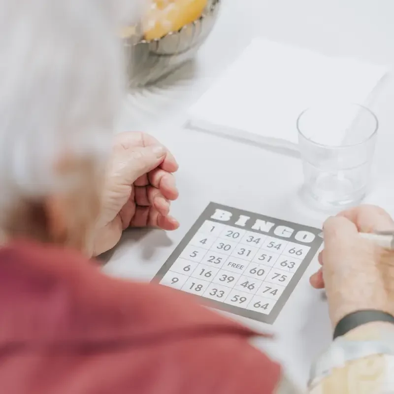 Person mit grauen Haaren hält eine Bingokarte mit Zahlen in der Hand