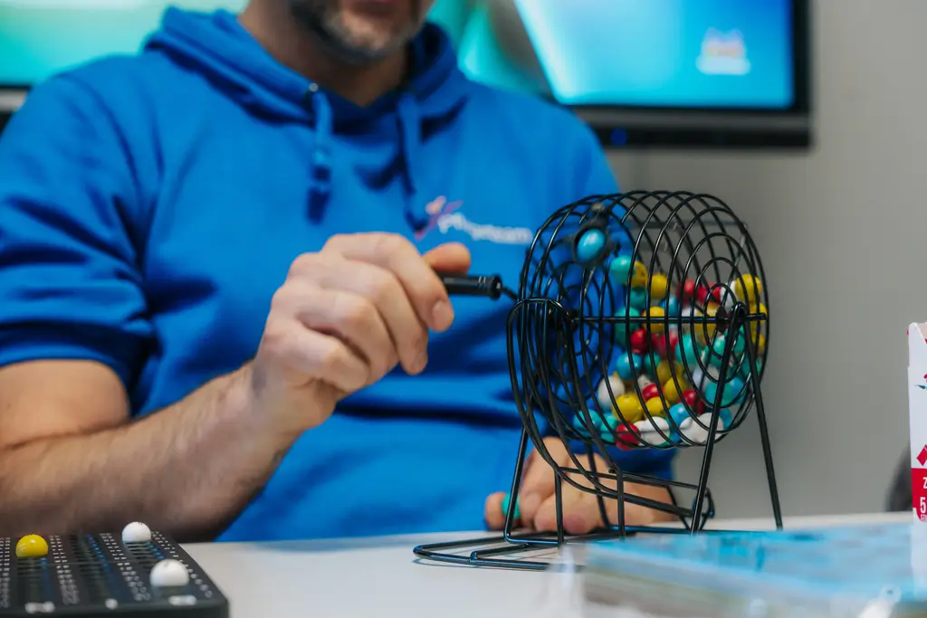 Person in blauem Kapuzenpullover dreht an einem schwarzen Metallgitter mit bunten Kugeln in einem Bingospiel