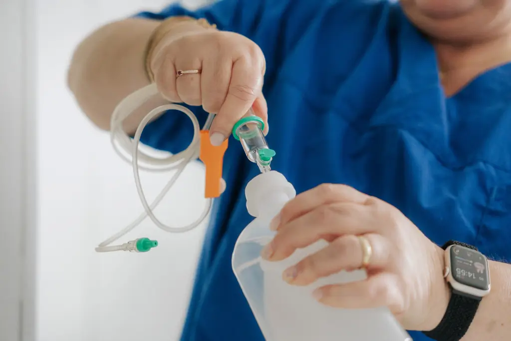 Nahaufnahme einer Person in blauer Kleidung, die einen Infusionsbeutel mit einem Schlauch verbindet