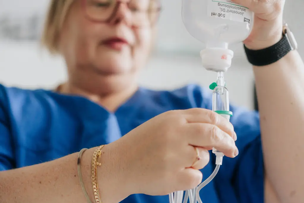Person in blauer Kleidung hält Infusionsflasche und Infusionsschlauch in den Händen