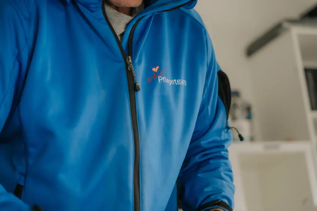 Oberkörper einer Person in blauem Reißverschlussjacke mit Logo 'meinPflegeteam'